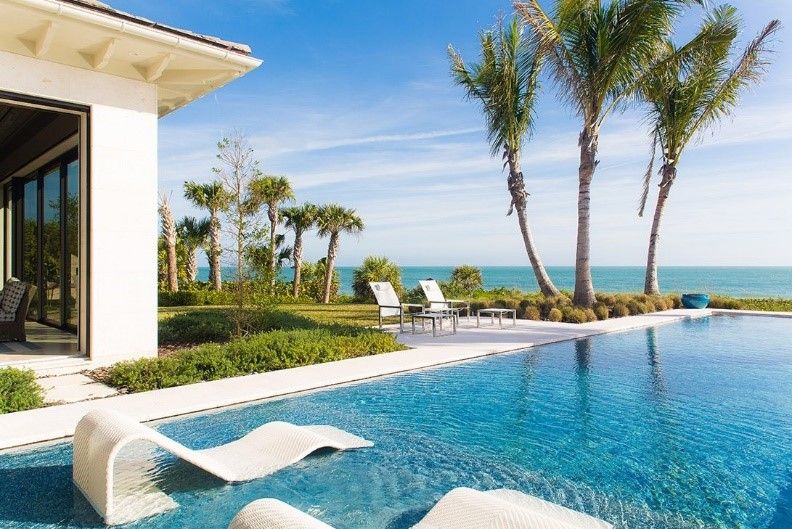 Lounge chairs partially immersed in a pool with an ocean view.